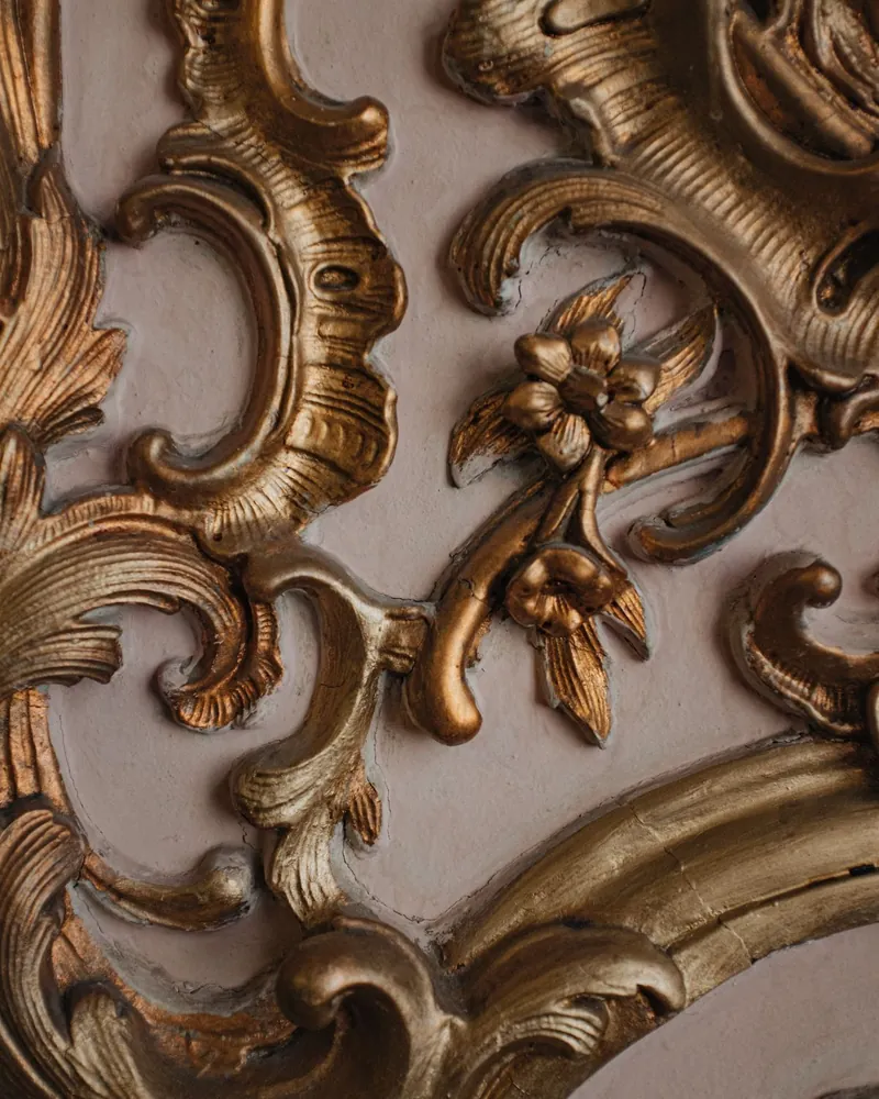 Detalle de talla dorada con roleos y flores, con desgaste del oro y el aparejo claro visible en los fondos